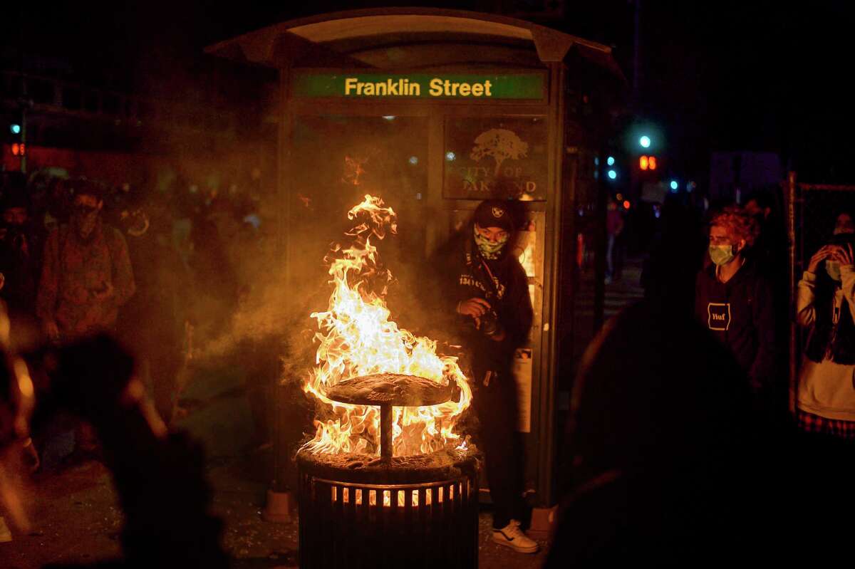 In this May 29, 2020, photo, a fire burns in a trash can as demonstrators protest in Oakland, Calif. against the Monday death of George Floyd, a handcuffed black man in police custody in Minneapolis.