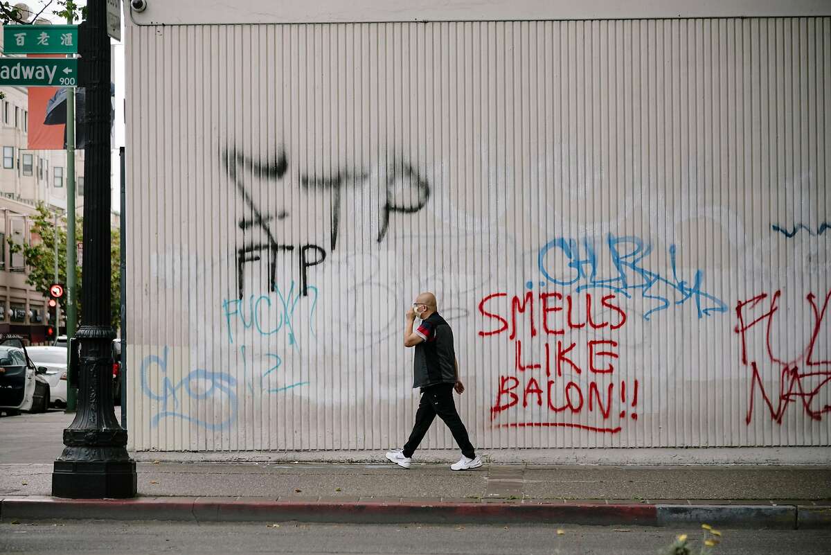 Man walks graffiti on a building on Broadway that was a result of overnight George Floyd protests in Oakland, Calif, on Sunday, May 31, 2020.