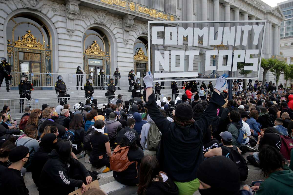 A protester holds a sign up as thousands gathered at City Hall took a knee and chanted for the police to do so as well in San Francisco, on Sunday, May 31, 2020.