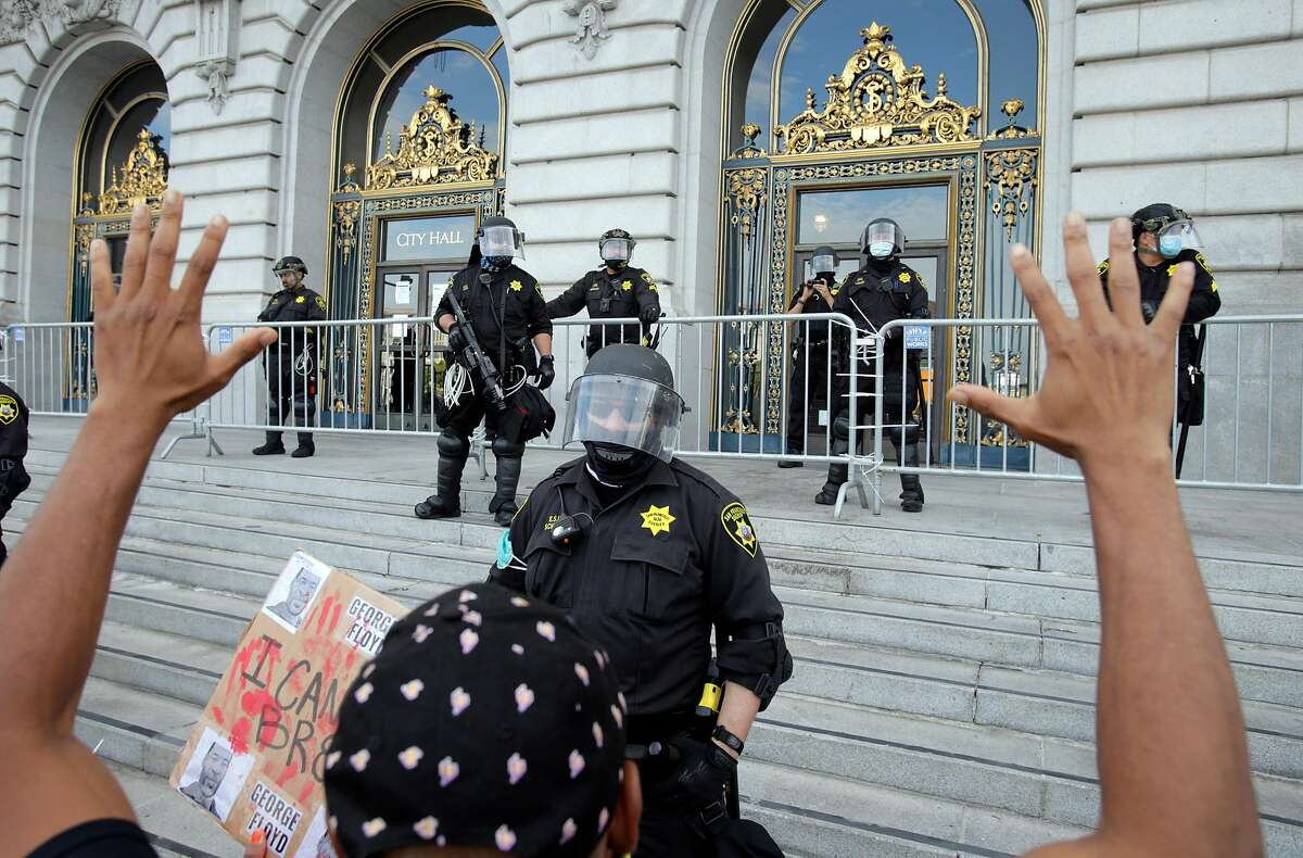 A row of San Francisco Sheriffs officers watch as a protester puts his hands up as thousands gathered at City Hall in San Francisco, Calif., on Sunday, May 31, 2020, for the third straight night of worldwide solidarity protests over the killing of George Floyd in Minneapolis by police earlier in the week.