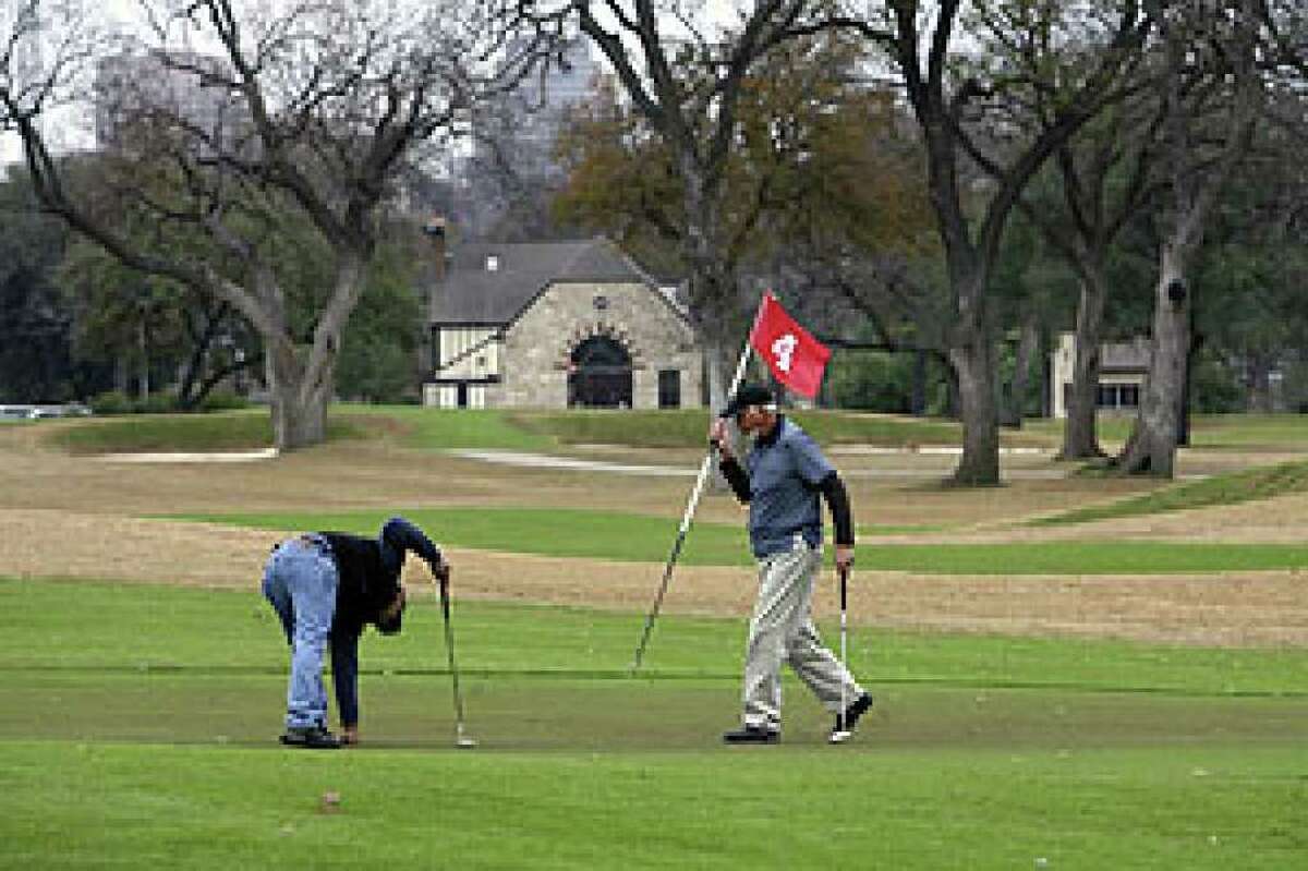 Tony Maciel (left) and John Browning finish playing No. 4 at Brackenridge, with its signature clubhouse in the distance, on a blustery Thursday.