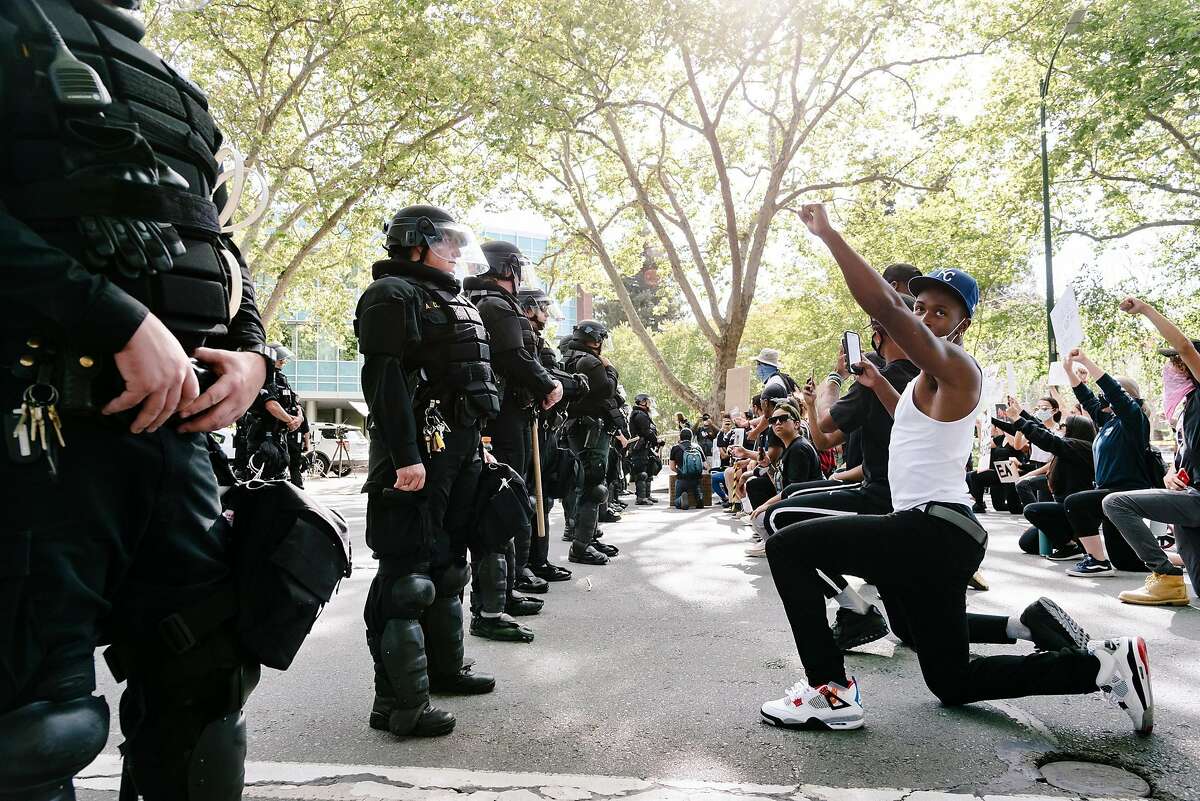 Kenroy Higgins of Oakland and other protestors take a knee and hold up their fists in front of a line of police officers in riot gear blocking North Broadway near the Walnut Creek Police Station as protestors gather for a George Floyd Solidarity Demonstration at nearby Civic Park in Walnut Creek, Calif, on Monday, June 1, 2020.