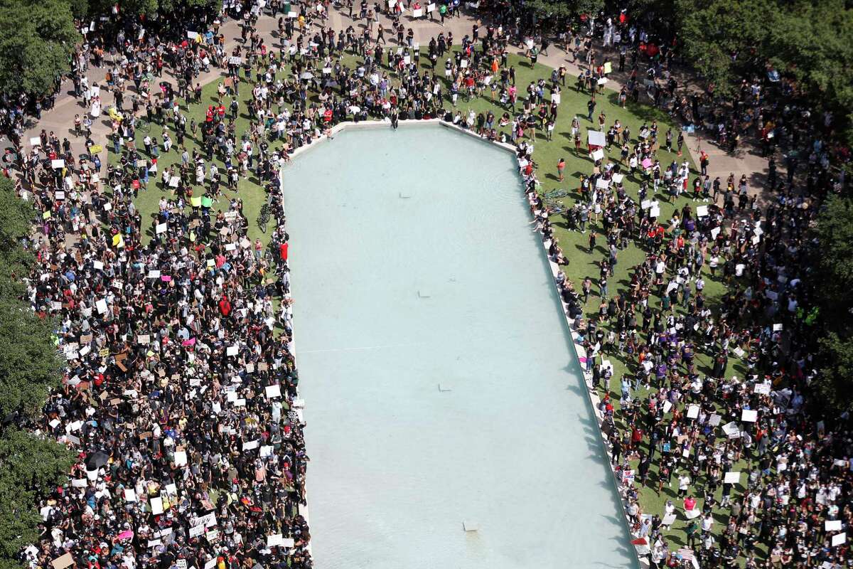 People stand on the grassy area near the reflection pond as they joined George Floyd’s family in a march on Tuesday, June 2, 2020, from Discovery Green to City Hall in downtown Houston.