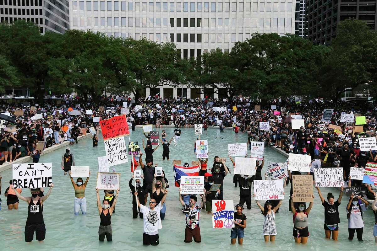 Protesters hold signs in the reflecting pool in front of Houston's City Hall as they listen to speeches after a march in honor of George Floyd on Tuesday, June 2, 2020.