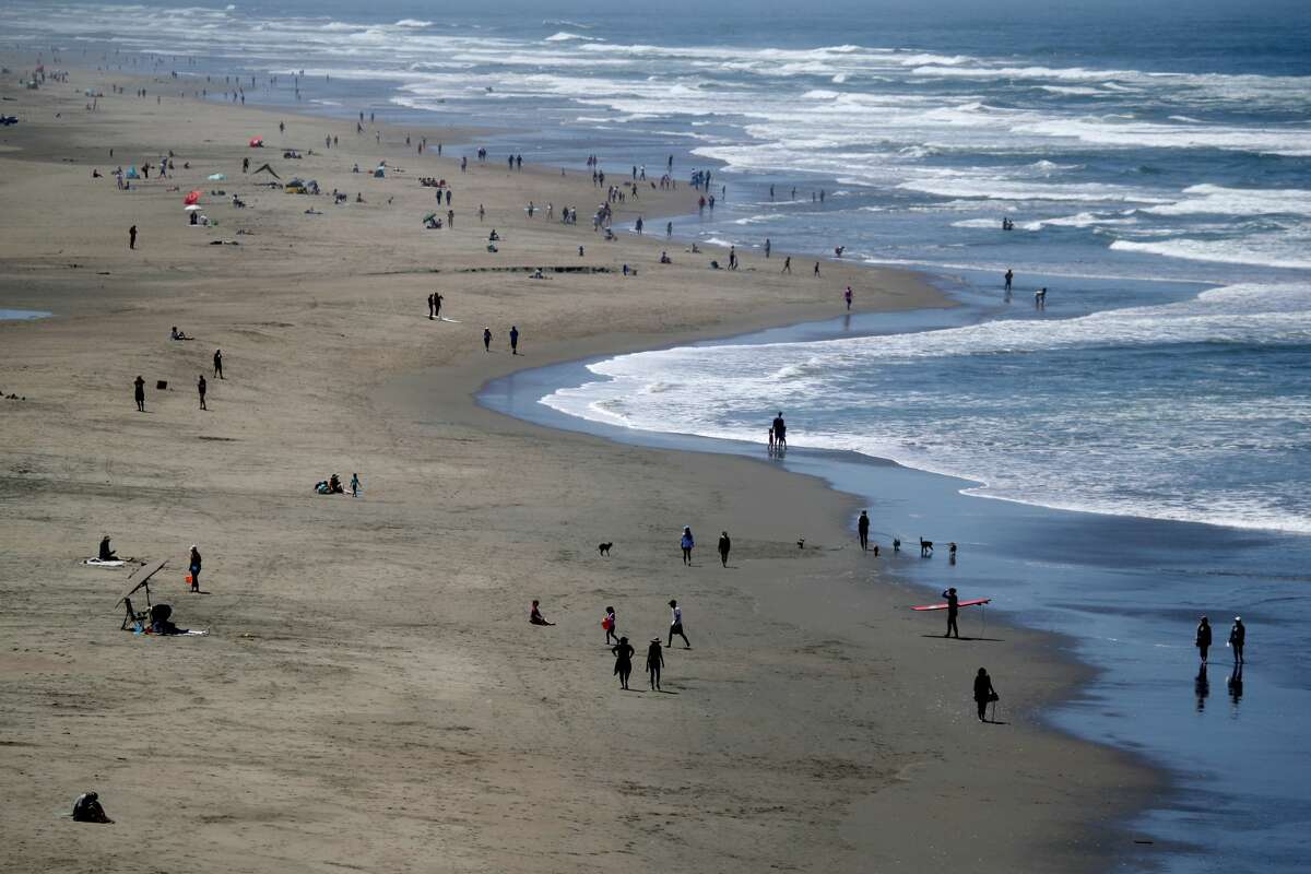 FILE - People walk along Ocean Beach on May 26, 2020 in San Francisco, California. The beach's parking lots were closed for the remainder of the weekend after over a thousand people were seen gathering there to celebrate Burning Man on Saturday.