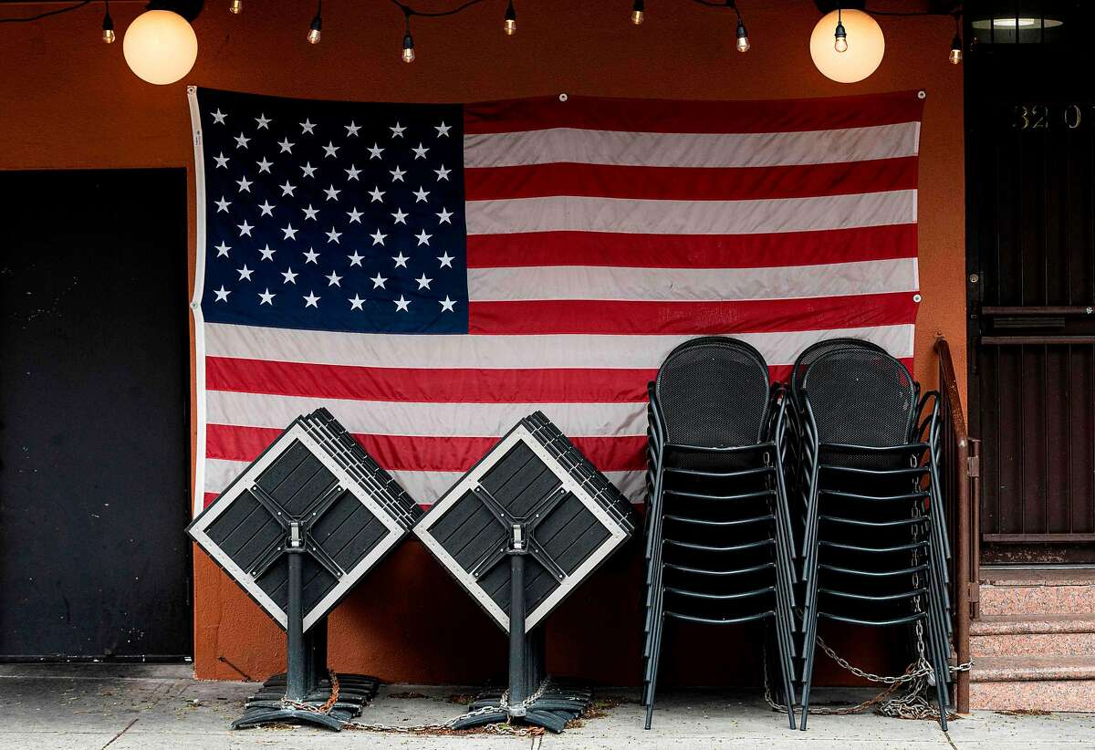 Chairs and tables are stacked in front of an American flag at a closed restaurant in New York on April 27 during the coronavirus pandemic.