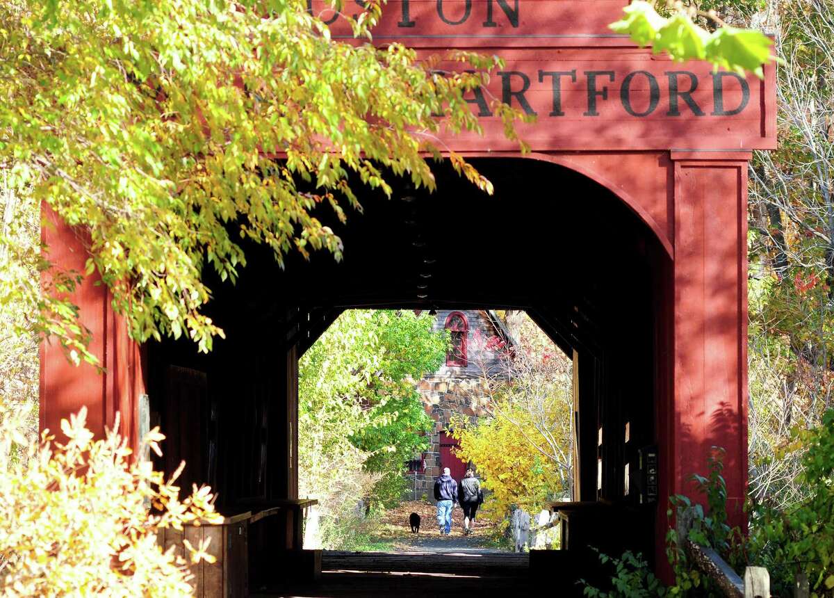 A couple walks a dog into East Rock Park past a covered bridge next to the Eli Whitney Museum in Hamden, which offers an online program these days.