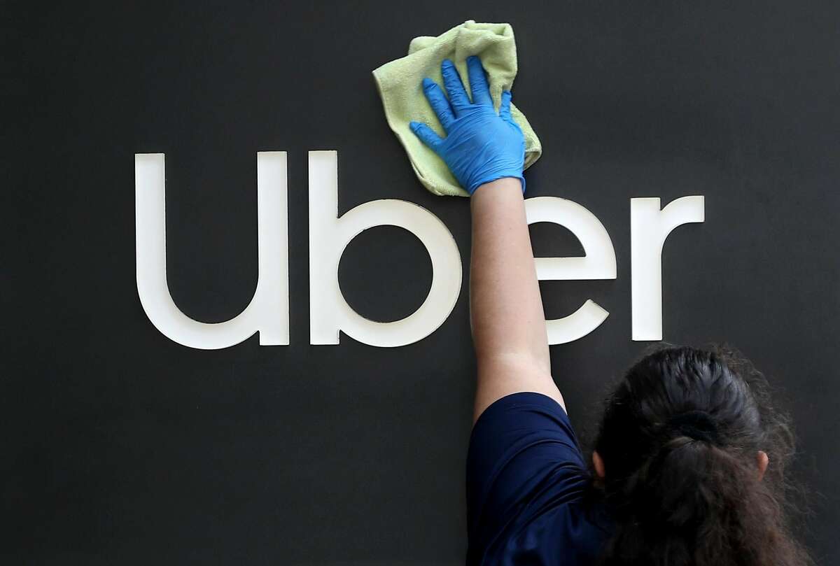 A worker cleans a sign in front of Uber headquarters in San Francisco earlier this year. Uber, Lyft and other gig economy companies have spent an astounding $185 million to get voters to pass Proposition 22, would which would allow ride-hail and delivery drivers to continue to be treated as independent contractors.