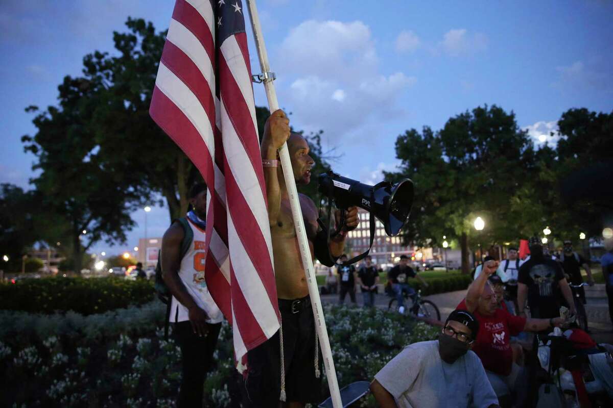 Carrying a U.S. flag, Jesus Perales, 38, offers words of encouragement to people gather in protest at Travis Park, Thursday, June 4, 2020. It is the sixth of protest in the police killing of George Floyd on Memorial Day in Minneapolis.