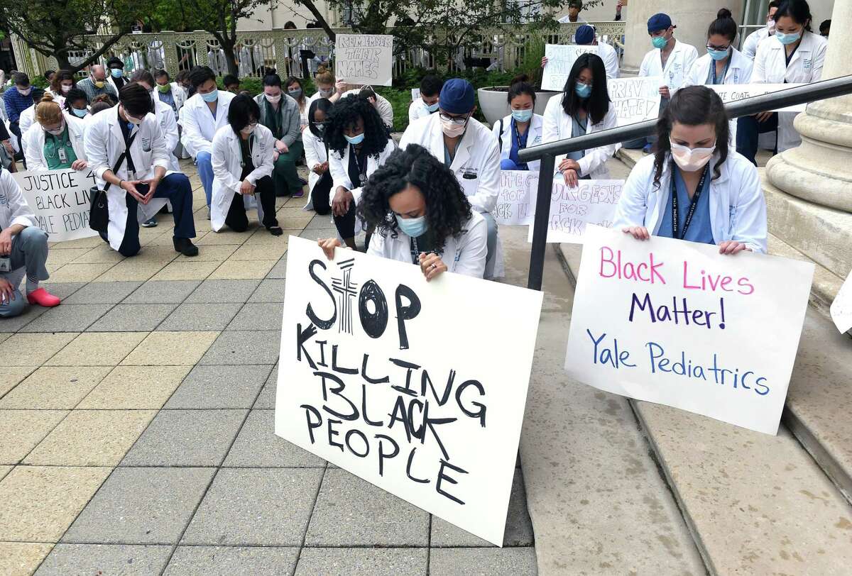 Protest organizers, Dr. Amanda Calhoun, center, and Dr. Molly Markowitz, right, take a knee with other hospital personel during a moment of silence at the White Coats for Black Lives demonstration in front of the Yale School of Medicine in New Haven on June 5, 2020.