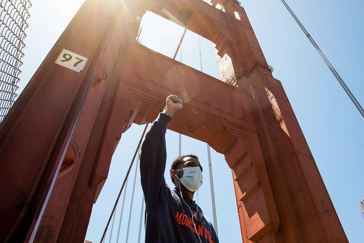 A demonstrator raises his fist in the air while sporting a mask as he makes his way with thousands of others across the Golden Gate Bridge in San Francisco, Calif. Saturday, June 6, 2020 during a march in support of the Black Lives Matter movement.