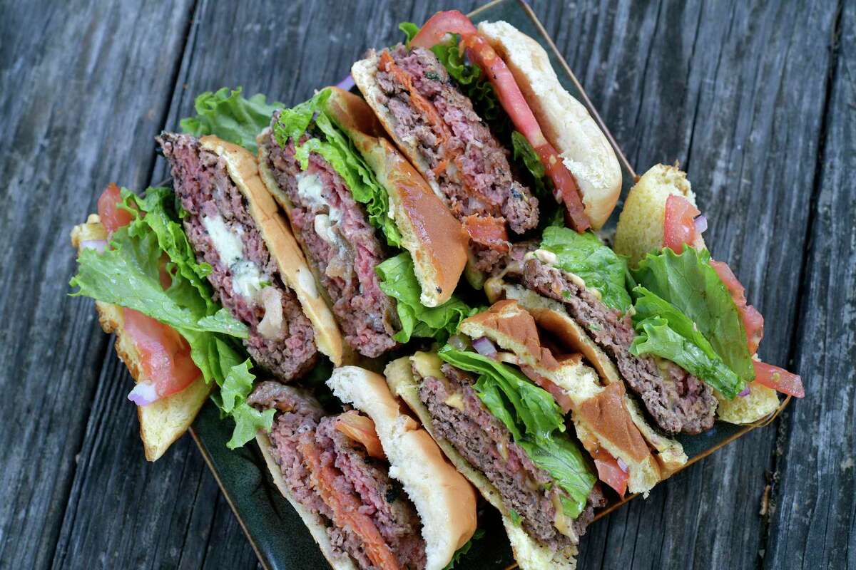 A lineup of stuffed burgers are finished off the grill.