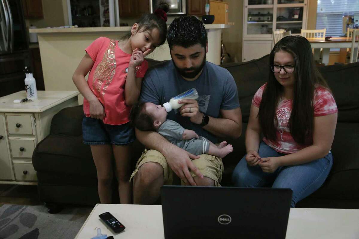 Brandon Beard, center, gathers the family around a laptop as they talk with his wife and their mother, Teresa Beard, during a video call from New York. Daughters, Alexis, 7, left, and Lillian, 15, right, and three-month-old son, Nolan, look forward to seeing their mother on video chats and count down the days until she returns.