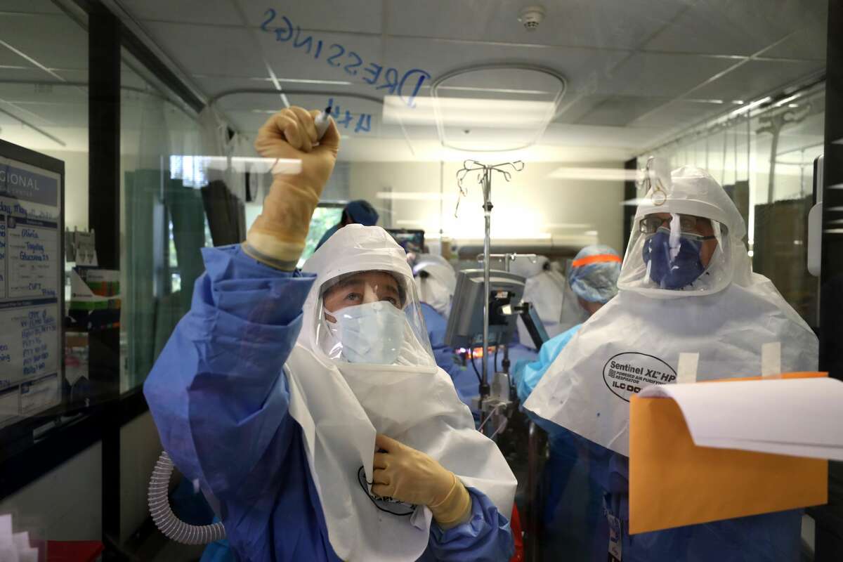 A nurse writes a note on a window as a team of doctors and nurses performs a procedure on a coronavirus patient in the intensive care unit (I.C.U.) at Regional Medical Center.