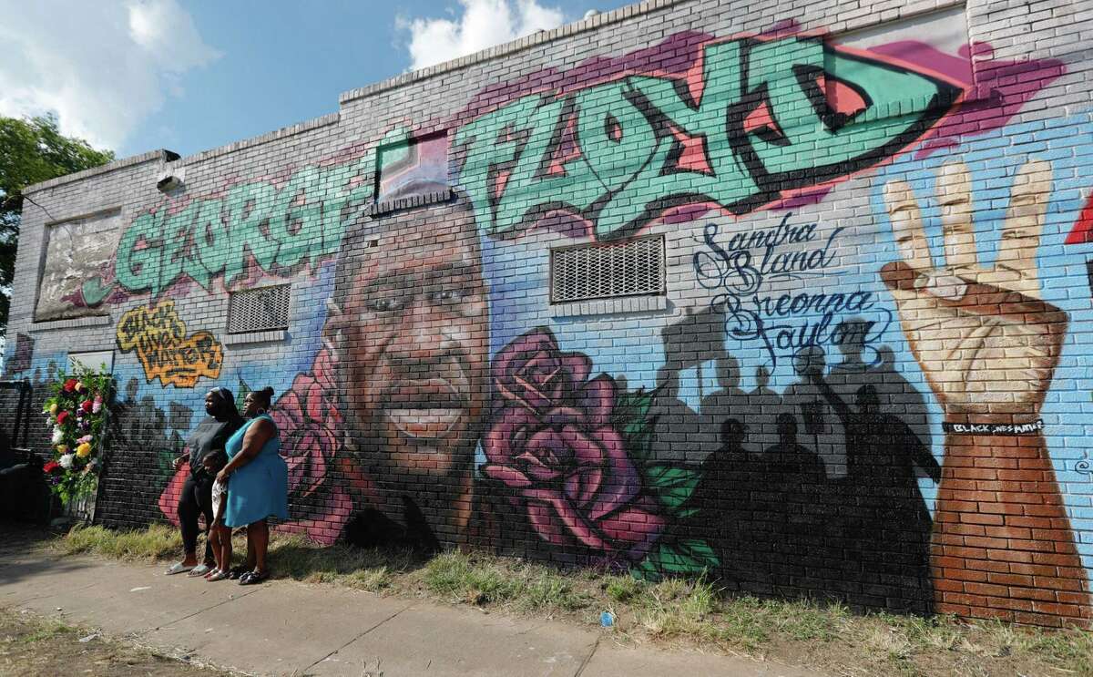 A family takes a photo in front of a mural in honor of George Floyd near the intersection of Elgin Street and Ennis Street, Monday, June 8, 2020, in Houston.
