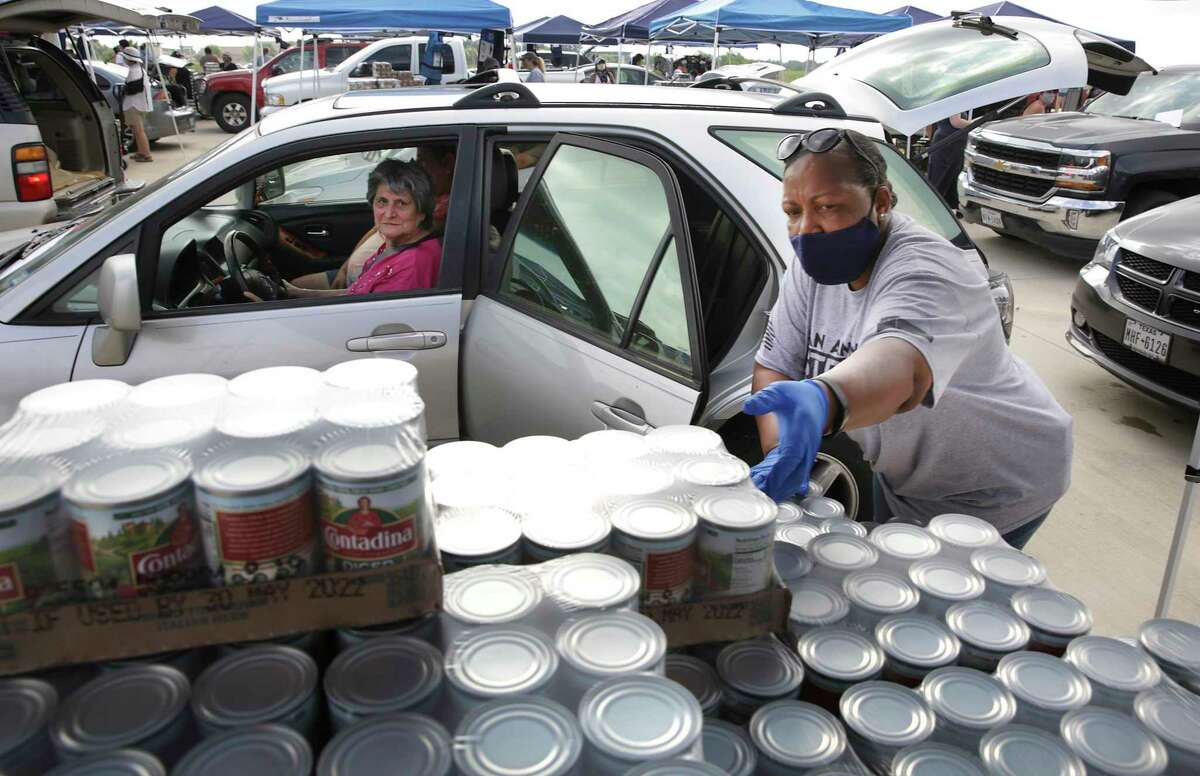 Volunteer Glenda Henry, right, reaches for a box of canned tomatoes for Lorenza Flores, in vehicle, at the San Antonio Food Bank’s “Day of Service” to honor George Floyd during a food distribution event at Traders Village, on Tuesday, June, 9, 2020.