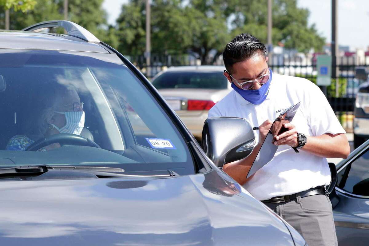 CarMax appraisal specialist Jose Ayala talks with the owner of a Lexus SUV as she sits in the driver seat while he gets initial information on the vehicle brought in for possible sale Monday, June 8, 2020 in Houston, TX. CarMax has instituted a “limited touch” system that reduces contact with both the owners and vehicles as a result of the COVID-19 pandemic.