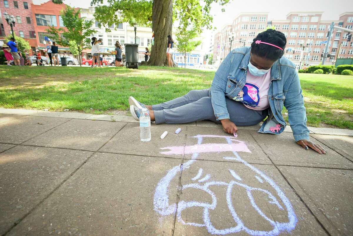 Codi-Ann Montaque, of Stamford, quietly draws a fist on a sidewalk while others nearby craft “Hearts for (George) Floyd” with hand-written messages that would be displayed on businesses surrounding Columbus Park in Stamford on Wednesday.