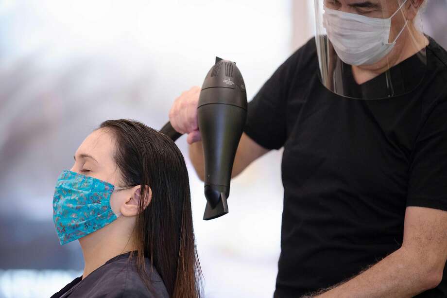 Stylist Neck Gunes (R) blow dries his customer Jennifer Nardelli's hair while wearing a face mask and shield at Saint Germain Hair Salon in Washington, DC, on May 29, 2020, as the District's phase 1 reopening plan begins. - Friday marks the beginning of phase one for the District of Columbia following the stay at home orders from the COVID-19 pandemic. (Photo by JIM WATSON / AFP) (Photo by JIM WATSON/AFP via Getty Images) Photo: Jim Watson / AFP / Getty Images