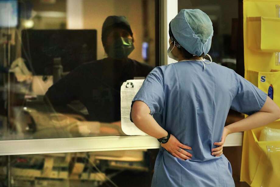 Nurse Evelyn Menking watches a COVID-19 patient through a window in the ICU of Northeast Baptist Hospital. The risk of infection keeps nurses at arm’s length from those under their care. Photo: Bob Owen / ©2020 San Antonio Express-News