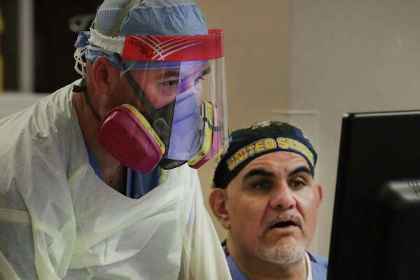 Wearing full protective gear, nurse Simon Denton, left, and Garcia look over information for a COVID-19 ICU patient.