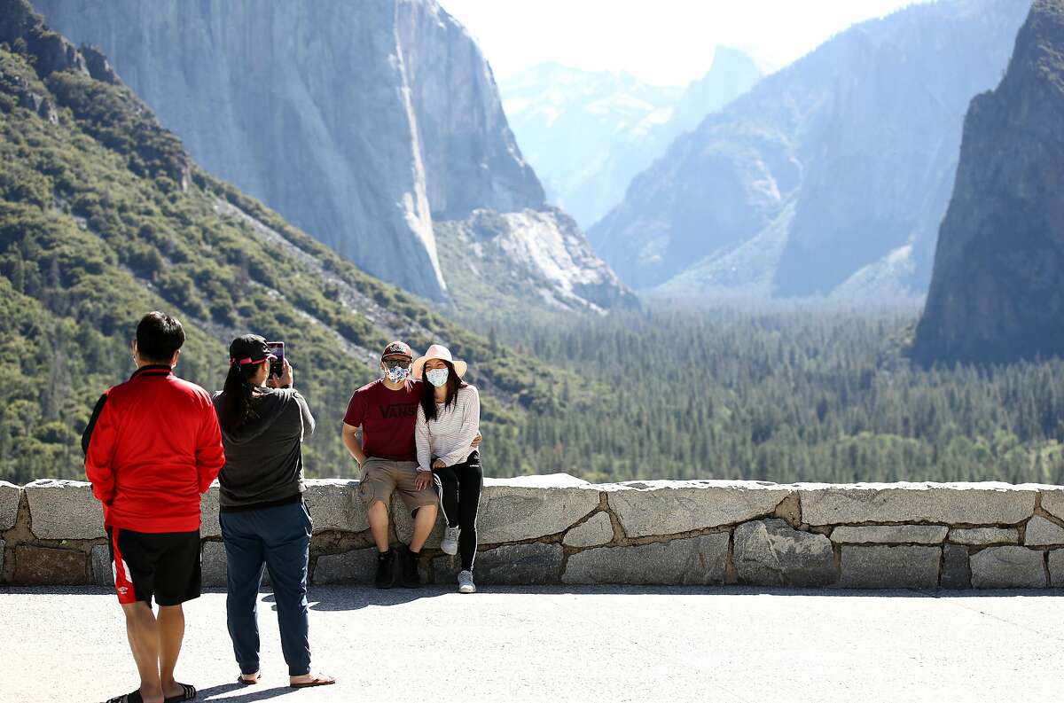Visitors, wearing masks for safety, take pictures at the Tunnel View lookout.