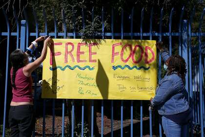 Oakland school district administrators Carmelita Reyes (left) and Cassaundra Reed post a sign at the Esperanza Elementary School food distribution site.