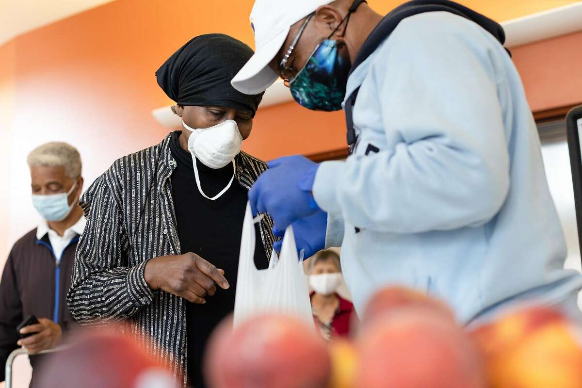 Geoffrey Grier (right), a staff member with the Bayview Senior Services, packs a bag with fruit for Nettie Fabian at Dr. George W. Davis Senior Center on Friday, June 12, 2020, in San Francisco, Calif.