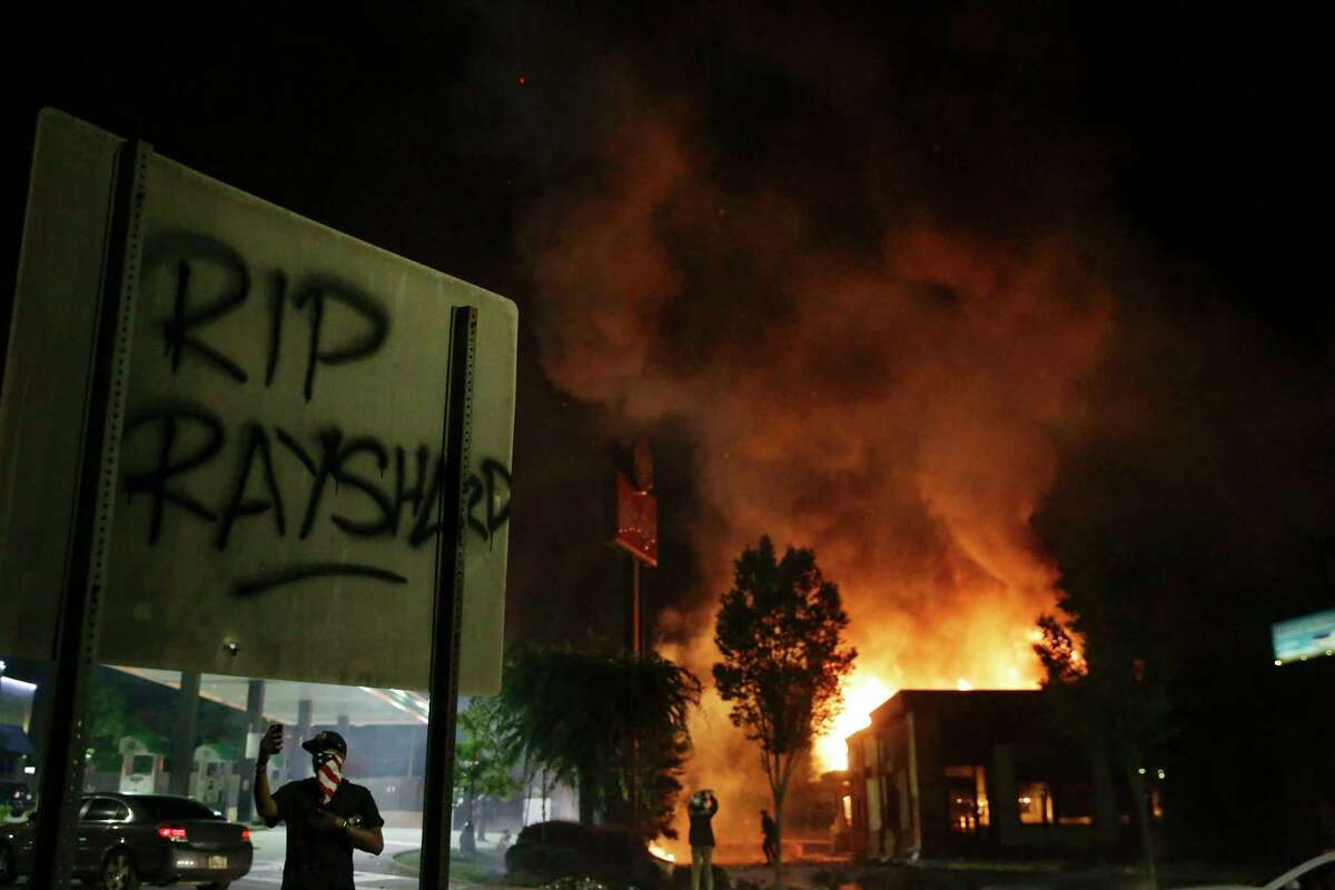 "RIP Rayshard" is spray painted on a sign as as flames engulf a Wendy's restaurant during protests Saturday, June 13, 2020, in Atlanta. The restaurant was where Rayshard Brooks was shot and killed by police Friday evening following a struggle in the restaurant's drive-thru line. (AP Photo/Brynn Anderson)