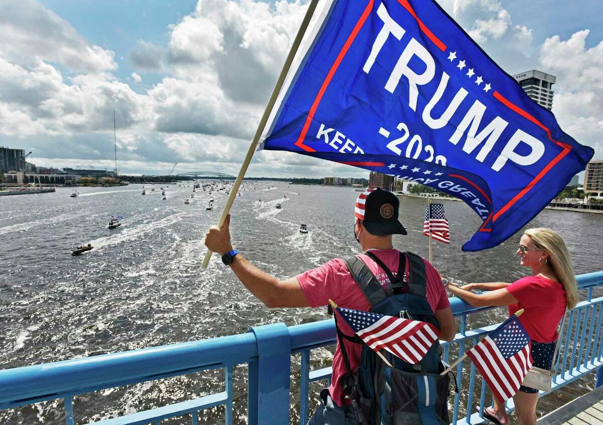 Brian Masotti, left, and Tracey Warren wave flags at the hundreds of boats idling on the St. Johns River during a rally Sunday, June 14, 2020, in Jacksonville, Fla., celebrating President Donald Trump's birthday. (Will Dickey/The Florida Times-Union via AP)