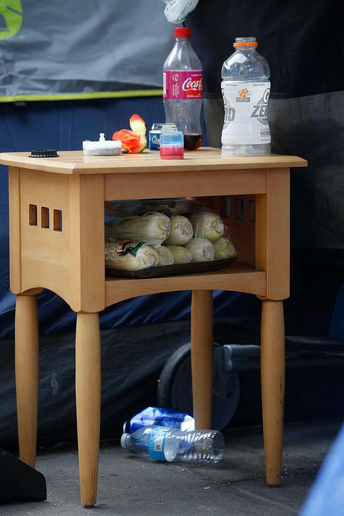 A side table next to a tent is seen with corn stored inside it and empty bottles and other items on top of it on Larch Street on Monday, June 15, 2020 in San Francisco, Calif.