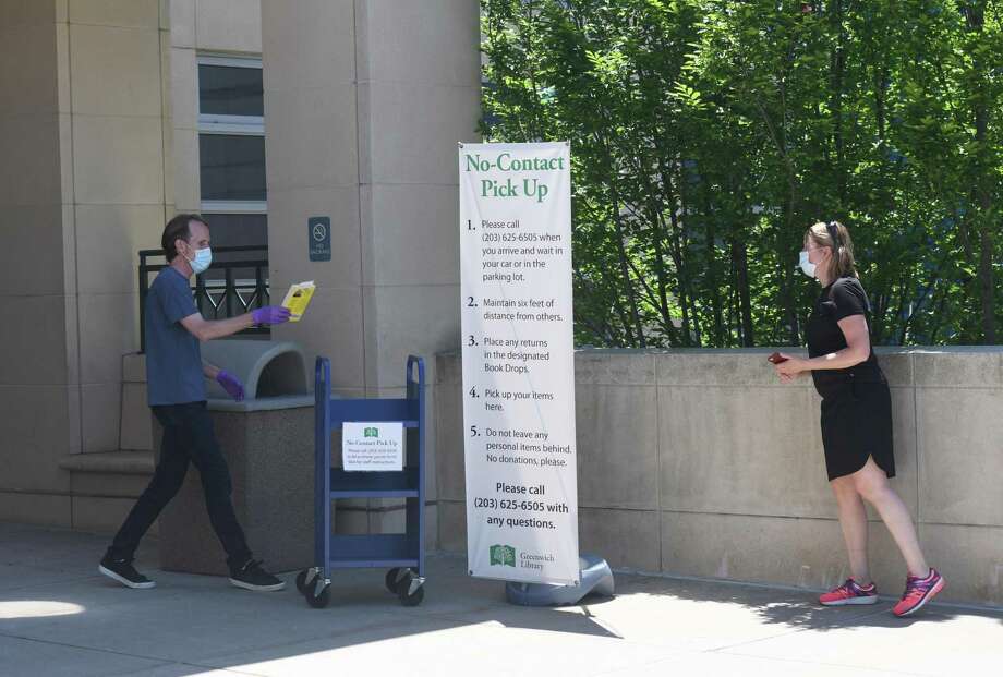 Library Technical Assistant Everett Perdue places a book on a cart for Cos Cob’s Kathy Myer as part of the new no-contact pick up process at Greenwich Library in on Tuesday. The library began the first step of returning to in-person services by offering no-contact pick up for library books and materials. Photo: Tyler Sizemore / Hearst Connecticut Media / Greenwich Time