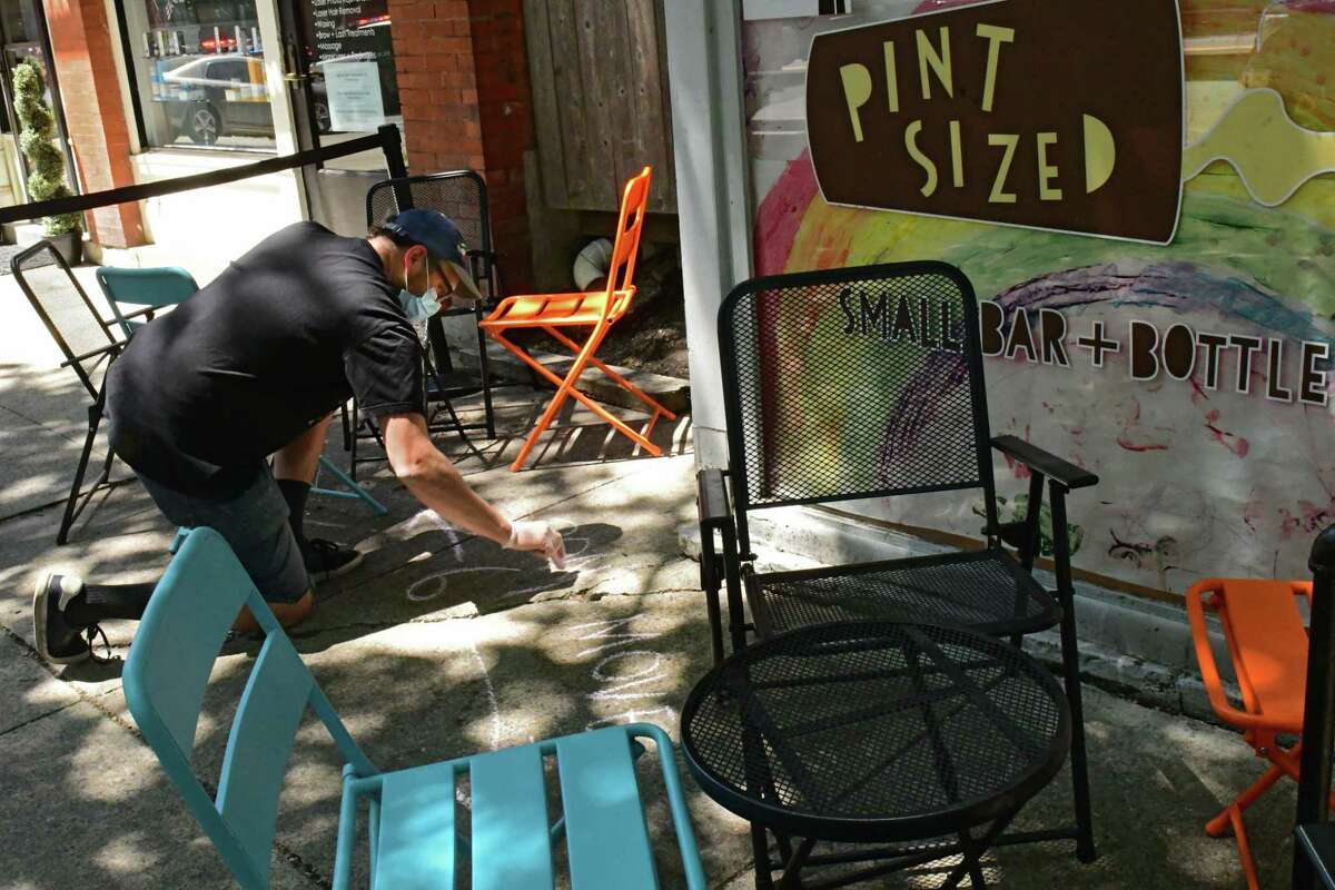 August Rosa, owner of Pint Sized, writes the message "Don't Move, 6 feet" with chalk between tables outside his craft beer establishment on Broadway on Wednesday, June 17, 2020, in Saratoga Springs, N.Y.  (Lori Van Buren/Times Union)