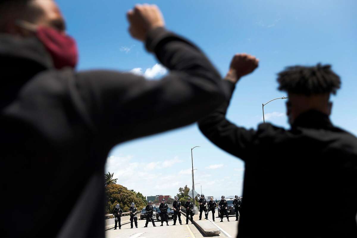 Two protesters march towards a group of California Highway Patrol officers blocking their entrance to I-880 during a protest march that started at Oakland Police Headquarters in Oakland, Calif., on Sunday, June 7, 2020.