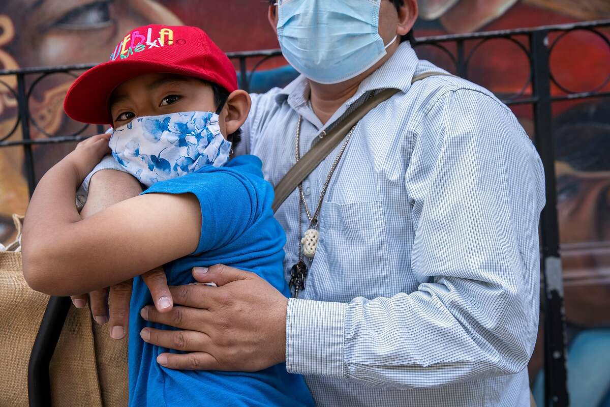 From left: Angel Pascual, 6, is embraced by his father Alejandro Pascual along 24th Street as they wait for Angel's mother to come back from a store, Thursday, May 7, 2020, in San Francisco, Calif. Alejandro was laid off as a restaurant cook after the restaurant boarded up, amid the coronavirus pandemic. Alejandro's partner Asuncion Morales is also without work. They said if they can't get their jobs back or if they can't find a new job soon their savings will deplete within months.