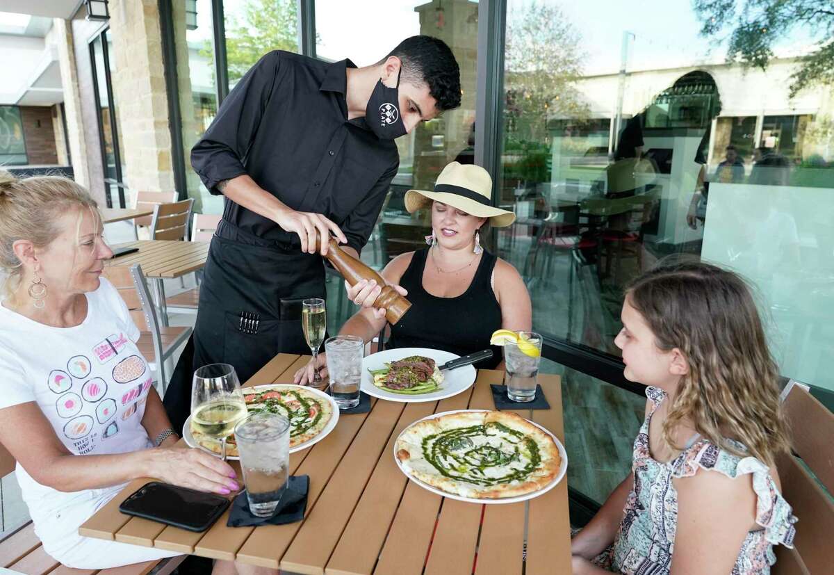 Gabe Rosado, server, adds pepper to dishes at the table of Kitty Weigel, left, Nicole Varick, center, and her daughter, Tinsley Varick 10, at The Union Kitchen, 9920 Gaston Rd., Thursday, June 18, 2020, in Katy.