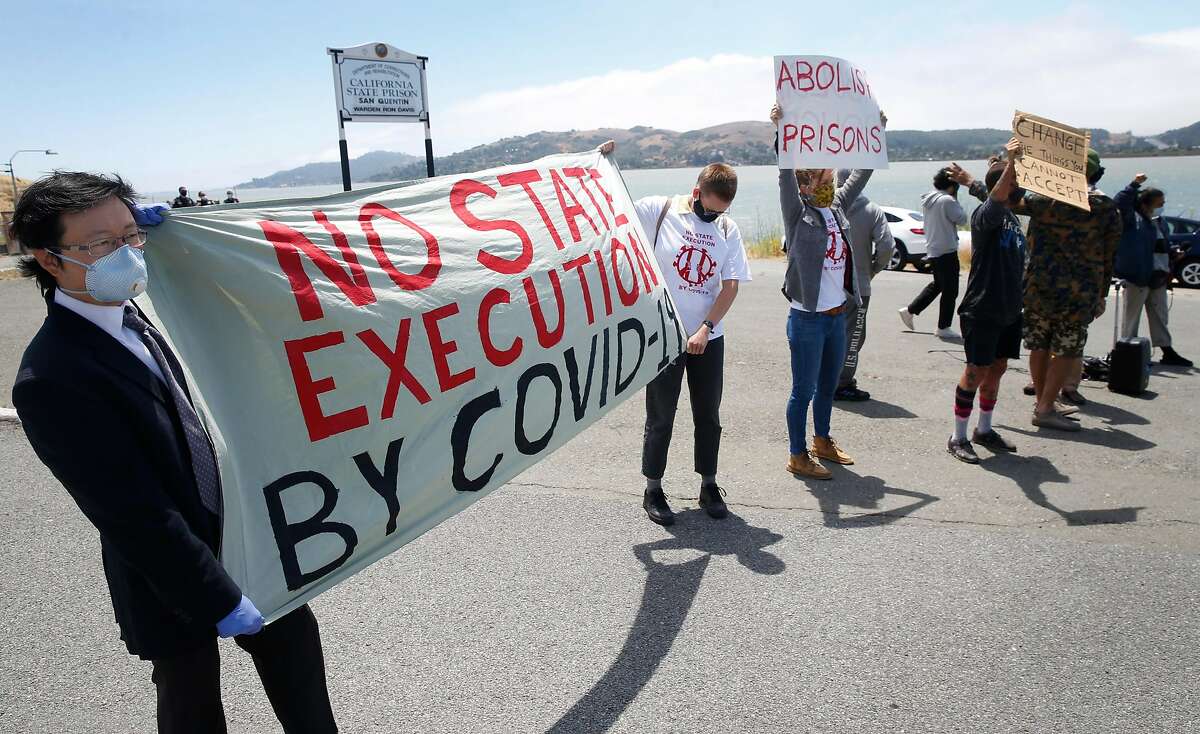 Richard Tan (left), co-organizer of the event, and Kayla Hunnewell display a banner as a caravan of cars carrying more than 200 protesters drives past the west gate of San Quentin State Prison in Larkspur, Calif. on Saturday, June 20, 2020 to demand protection for prisoners after COVID-19 cases exploded at San Quentin after the transfer of infected prisoners from Chino.
