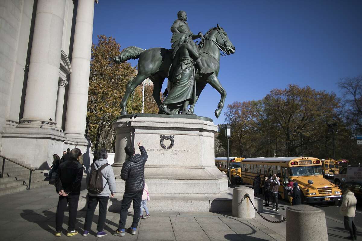 In this Nov. 17, 2017 file photo, visitors to the American Museum of Natural History in New York look at a statue of Theodore Roosevelt, flanked by a Native American man and African American man. The statue will be coming down after the museum's proposal to remove it was approved by the city (AP Photo/Mary Altaffer, File)