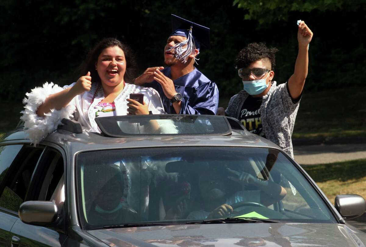 Graduates Miliana Herrera, left, and Ricardo Perez Santana sing along to music playing in the car as they arrive to get their diplomas during Ansonia High School's Commencement Exercises in Fairfield, Conn., on Saturday June 20, 2020. At right is Ricardo's brother Leonardo Perez Santana. School districts are planning for a 2021 graduation that may — or may not — be in person.