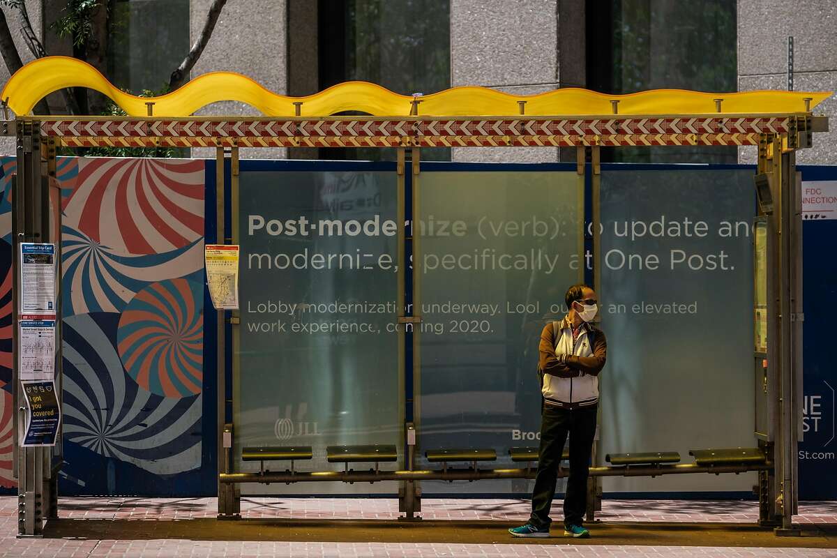 A public health banner displaying the requirement that masks be worn is seen on the side of a MUNI bus as a man wearing a mask passes by the other side in downtown San Francisco on Thursday, May 21, 2020.
