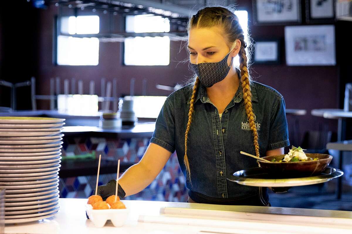 Evelyn Bruce sports a mask and gloves while serving food to customers at Teleferic Barcelona in Walnut Creek, Calif. Tuesday, June 9, 2020. They Bay Area is opening at a fairly fast pace, with Contra Costa County announcing plans this week to reopen indoor dining and hair salons soon, while it reports near-record new cases.