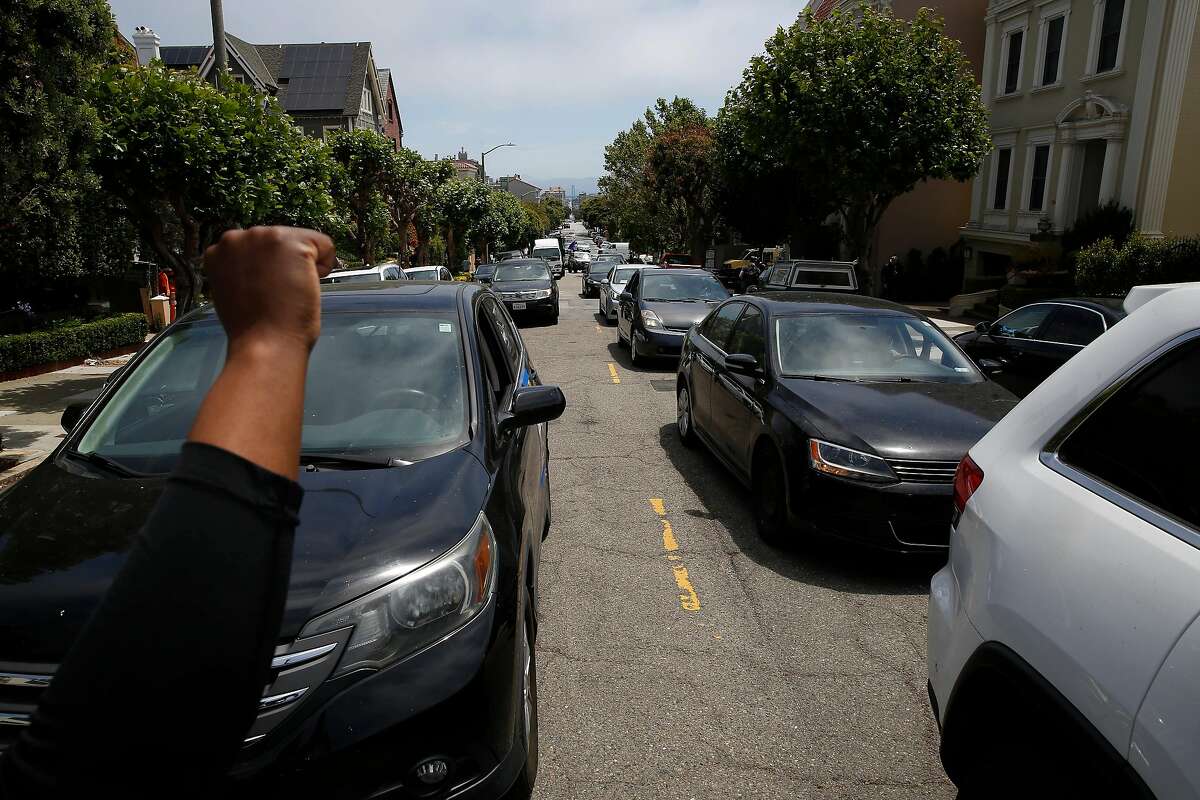 2020年6月24日星期三，在加利福尼亚州旧金山，当人们开车离开优步首席执行官达拉·科斯罗萨西的家前举行的抗议活动时，“Gig Workers Rising”的组织者切里·墨菲部长(左)向司机的大车举着手。