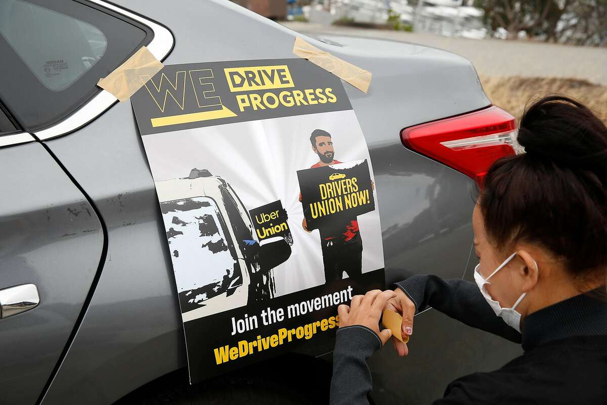 Saori Okawa, who drives for Uber, tapes a poster to the car of Rosa Mendoza at the Marina Green before the driver caravan protesting Uber's "refusal to obey basic labor protections for drivers” on Wednesday, June 24, 2020 in San Francisco, Calif.