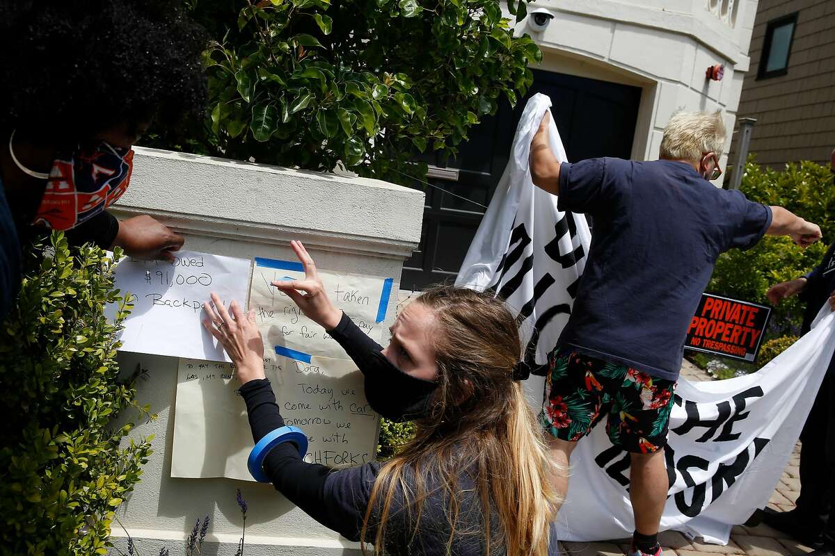 Minister Cherri Murphy (left), and Lauren Casey (second from left), both Gig Workers Rising organizers, post “grievance notes” on a post at the front of Uber CEO Dara Khosrowshahi’s home during a driver caravan protest on Wednesday, June 24, 2020 in San Francisco, Calif.