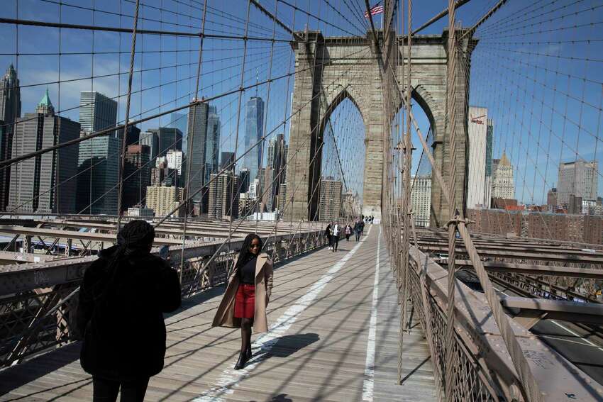FILE - In this March 16, 2020 file photo, tourist Ines Tshiyomba, center, poses as her friend Garethe Mawonso takes her photo on the Brooklyn Bridge in New York. New York, Connecticut and New Jersey will require visitors from other states with high infection rates to quarantine for 14 days. New York Gov. Andrew Cuomo announced the