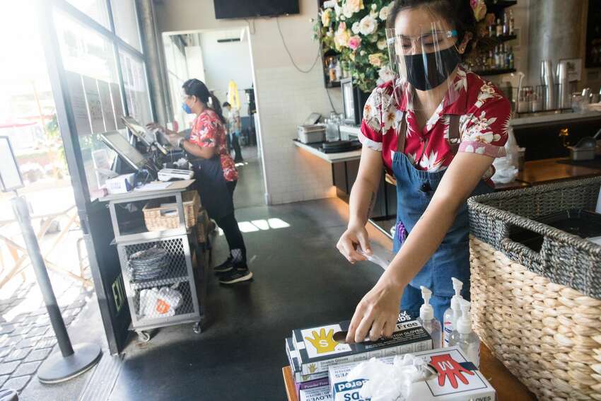 Waitress Jariya Namwaan disinfects her hands and puts on new safety gloves after cleaning a dining table. Namwaan works a shift at Farmhouse Kitchen in Oakland, Calif. on June 23, 2020. The restaurant recently re-opened to customers for outdoor dine-in service.