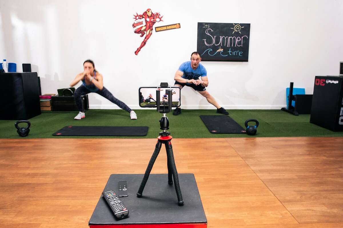 Trainer Justyna Sproull, left, and J.J. Miller, founder of The Firm Fitness, lead an online fitness class over Zoom streamed with a mounted phone on Wednesday, June 10, 2020 in San Francisco, California.