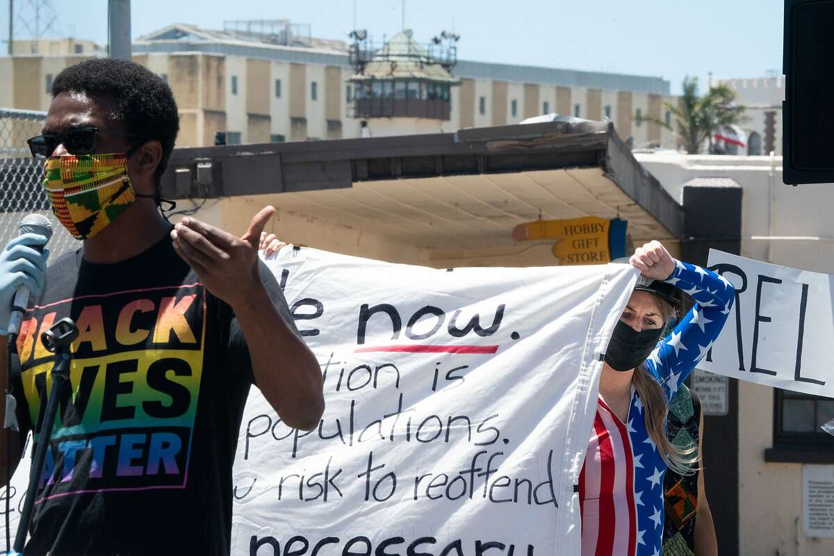 Speaker Emile DeWeaver, left, speaks as Jessica McKellar, right, helps holds a banner at the Stop San Quentin Outbreak rally at the prison gates on Sunday, June 28, 2020 in San Rafael, Calif.