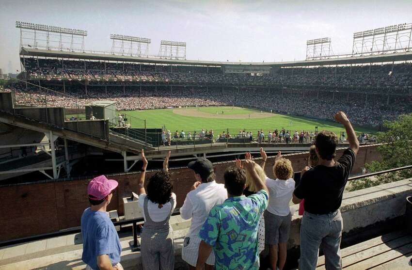 FILE - In this Monday, July 9, 1990, file photo, spectators watch an All-Star Game practice session from the roof of a building just outside Chicago's Wrigley Field. This week, Major League Baseball players and owners reached an agreement to play an abbreviated, 60-game season that would start July 23 or 24 in teamsa€™ home ballparks. But the seats will be empty. Instead, fans hoping to see a game in person will be have to settle for pressing their faces up against hotel windows, squinting through metal grates or climb to rooftops when baseball returns this month in otherwise empty stadiums. (AP Photo/Seth Perlman, File)