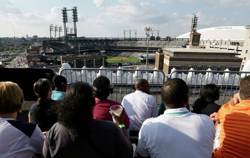 FILE - In this July 12, 2013, file photo, baseball fans watch from the roof of the Detroit Opera House before a baseball game between the Detroit Tigers and the Texas Rangers in Detroit. This week, Major League Baseball players and owners reached an agreement to play an abbreviated, 60-game season that would start July 23 or 24 in teamsa€™ home ballparks. But the seats will be empty. Instead, fans hoping to see a game in person will be have to settle for pressing their faces up against hotel windows, squinting through metal grates or climb to rooftops when baseball returns this month in otherwise empty stadiums. (AP Photo/Carlos Osorio, File)